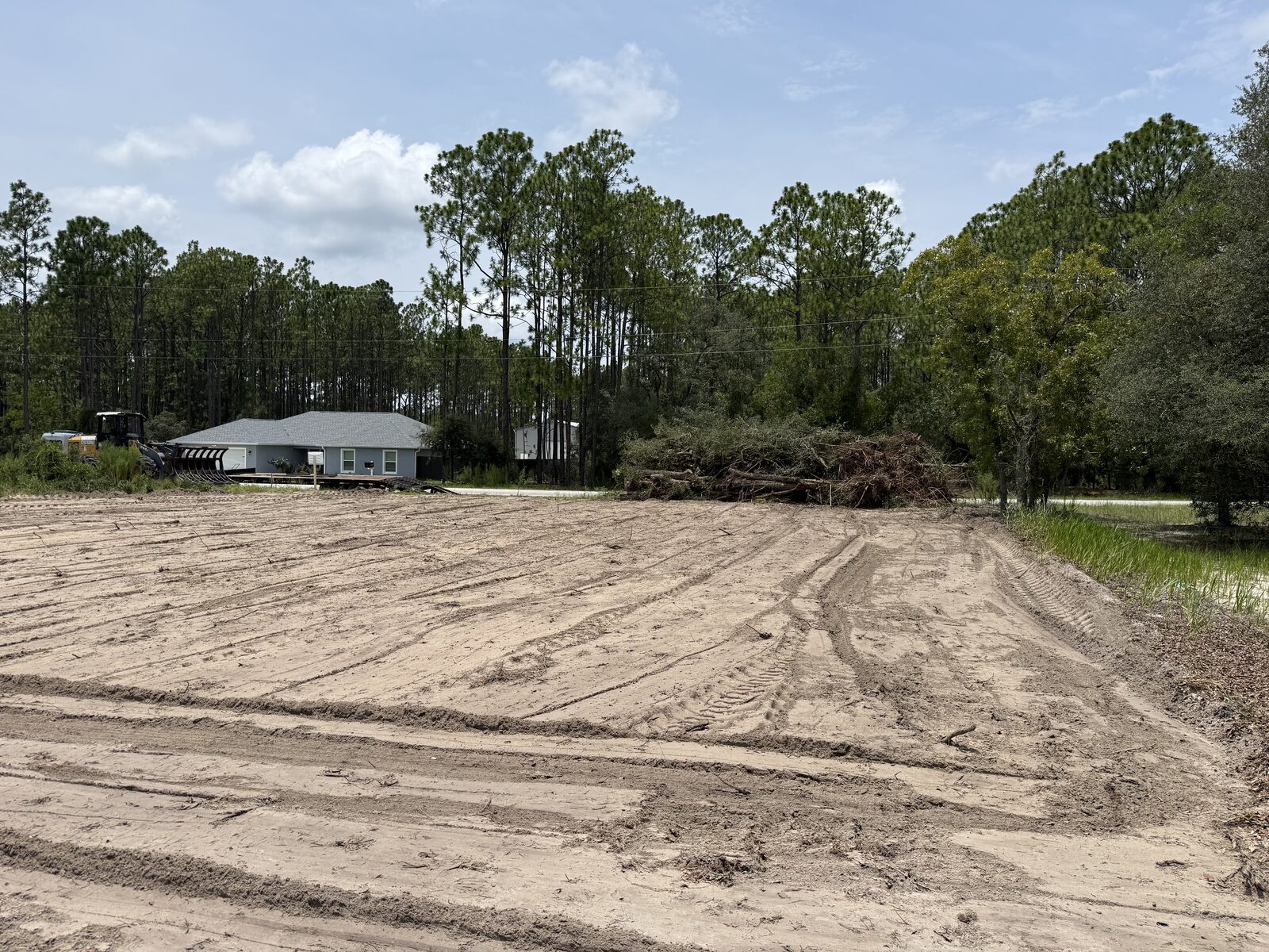 Cleared sandy lot with brush and tree debris staged near the edge